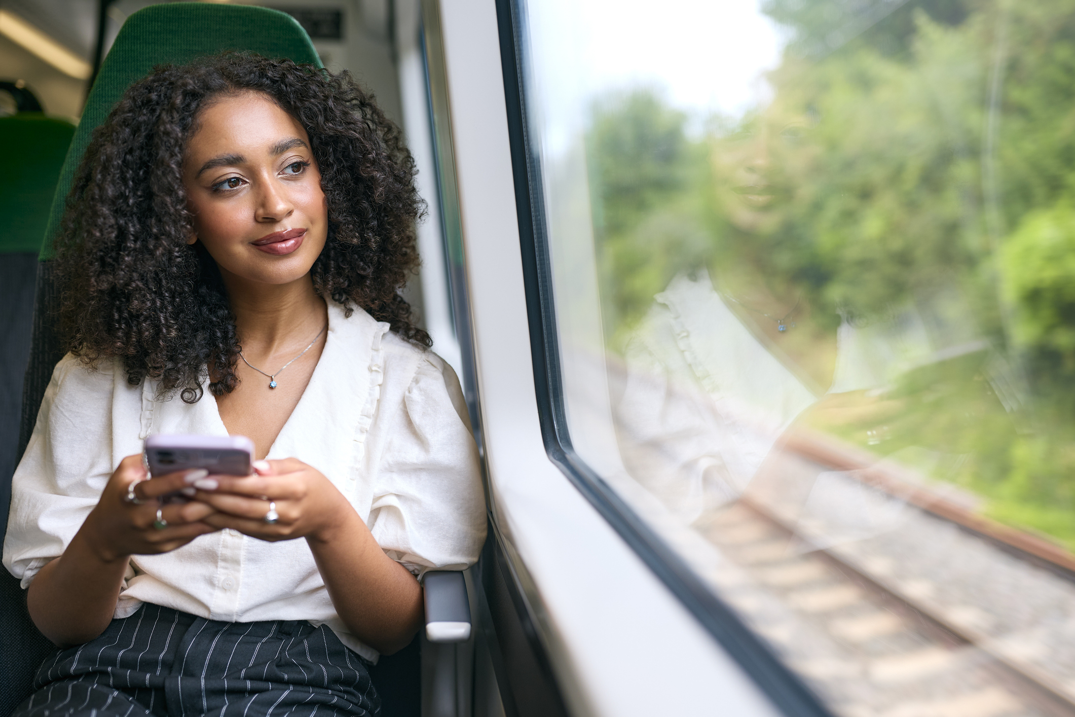 Young wioman ommuting To Work On Train Sitting Checking Messages Or Social Media On Mobile Phone